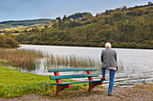Ein Mann steht auf einer Bank entlang des Ufers des Drinagh-Sees; Grafschaft Cork Irland