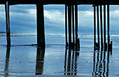 USA, California, Reflections on wet shoreline framed by silhouetted pier; Pismo Beach