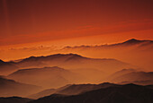 Nepal, Kathmandu-Tal, Blick von oben auf die Bergspitzen inmitten von orangefarbenem Dunst und Himmel.