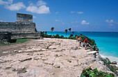 Mexiko, Yucatan-Halbinsel, Besucher stehen auf felsigen Klippen in der Nähe von Ruinen; Tulum.