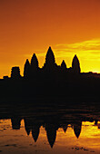 Kambodscha, Siem Reap, Angkor Wat, Silhouette eines Tempels bei Sonnenaufgang, Reflexionen auf der Wasseroberfläche, oranger Himmel