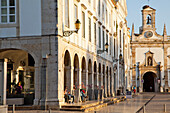 Ein Kirchengebäude und Menschen, die zwischen den Gebäuden spazieren gehen und sitzen; Faro Algarve Portugal