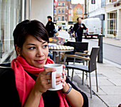 Woman Drinking Coffee At A Table On An Outdoor Patio; Cambridge England