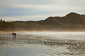 Ein Paar spaziert am Strand von Cox Bay bei Sonnenuntergang in der Nähe von Tofino; British Columbia Kanada