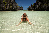 A Woman Tourist Wearing A Sun Hat And Bikini Relaxes In The Clear Waters Of Matinloc Island Near El Nido And Corong Corong; Bacuit Archipelago Palawan Philippines