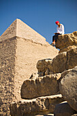 Eine weibliche Touristin liest einen Reiseführer, während sie vor den Pyramiden von Gizeh in der Nähe von Kairo sitzt; Gizeh Ägypten