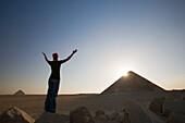 Eine junge Touristin hebt ihre Arme in Richtung der Sonne und der Roten Pyramide; Dashur Ägypten