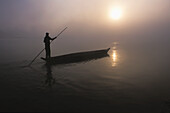 A Man Pushes His Dugout Canoe Along The Rapti River Near Sauraha And Chitwan National Park At Dawn; Nepal
