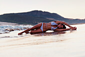 Eine Frau im Bikini liegt auf dem nassen Sand; Tarifa Cadiz Andalusien Spanien
