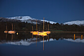 Schnee auf den Gipfeln der Berge, die sich im Wasser spiegeln, mit Booten, die im Lake Windermere festgemacht haben; Cumbria England