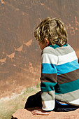 A Boy Sits On The Edge Of A Rock Looking Down Into A Canyon; Arizona United States Of America