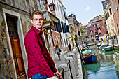 Ein junger Mann steht an einem Geländer an einem Kanal; Venedig Italien