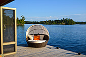 Ein gepolsterter Loungesessel auf einem hölzernen Dock am Rande des Wassers; Lake Of The Woods Ontario Kanada