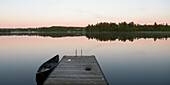 Ein Kanu im Wasser neben einem Dock bei Sonnenuntergang; Lake Of The Woods Ontario Kanada