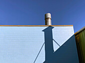 Metallabzugshaube auf dem Dach eines blauen Schlackenblockgebäudes, Schatten an der Wand