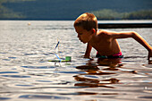 Junge mit selbstgebautem Spielzeug-Segelboot im See