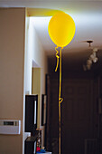 Yellow helium balloon with long string on apartment ceiling