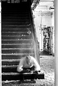 Transparenter Mann hockt auf der Treppe eines verlassenen Gebäudes