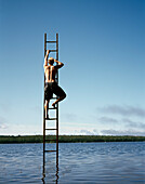 Rückansicht eines mittelgroßen Mannes, der auf eine Leiter in der Mitte des Sees steigt