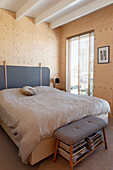 Double bed and bench in the bedroom with light-colored wood paneling