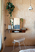 Small dressing table with vintage mirror in bedroom with light-colored wood paneling