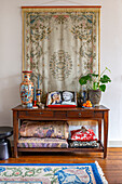 Table with blankets, cushions, porcelain vase, book and houseplant with a wall hanging above