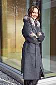 Young brunette woman in a gray wool coat with a fur collar and leather pants