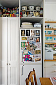 White cupboard with storage containers and bowls and fridge with colorful postcards