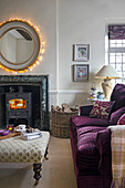 Wohnzimmer mit Kamin, rundem, beleuchtetem Spiegel und lila Sofa