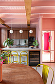 Kitchen in shades of pink with yellow bar stools and wooden elements