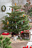 Weihnachtsdeko im Wintergarten, Kerzen, Papieranhänger und bemalte Zapfen vor geschmücktem Christbaum mit Hund
