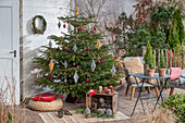 Weihnachtsdeko im Wintergarten, Kerzen und bemalte Zapfen vor geschmücktem Christbaum