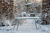 Verschneite Gartenbank im winterlichen Garten