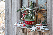 Verschneiter Winterstrauß am Fensterbrett, Kiefernzweige, Goldrute, Blaufichte, Lärche und Zierapfel, mit Schnee im Eimer