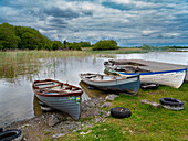 Boote warten auf Schiffer auf dem Lough Carra, Grafschaft Mayo, Irland. Ein Heiligtum wacht über die Fischer.