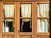 Italien, Toskana, Monticchiello. Gelbe Vorhänge hängen in einem Schaufenster.