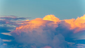 Bunte Wolken bei Sonnenuntergang im Kontrast zum tiefblauen Himmel, mit einer Gewitterwolke, die hinter einer linsenförmigen Wolke auftaucht.