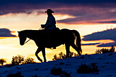 USA, Shell, Wyoming. Hideout Ranch cowboy on horseback silhouetted at sunset. (PR,MR)