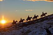 USA, Wyoming. Hideout Horse Ranch, wranglers on horseback in snow at sunset. (MR,PR)