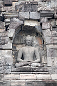 Indonesia, Java, Borobudur. Largest Buddhist monument in the world. UNESCO. Buddha statue in ornate wall.