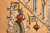 Italien, Umbrien, Assisi. Schmiedeeiserne Drachenlaterne an einer Mauer über einem Eingang.