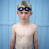 Portrait Of Young Boy In Swimming Goggles Against Blue Panel