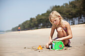 A girl makes sandcastles with a green bucket on Turtle Beach, Goa, India.