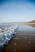Wellenplätschern am Sandstrand, an einem ruhigen sonnigen Tag in Putsborough Sands, Nord-Devon, Großbritannien