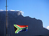 Südafrikanische Flagge weht über der Victoria and Albert Waterfront mit Kapstadt und dem Tafelberg dahinter, Südafrika.