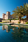 Marokko, Schwimmbad des Dar Ahlam Hotels mit Hauptkasbah im Hintergrund in der Morgendämmerung; Skoura