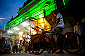 Mann verkauft Popcorn und Kind auf einem Fahrrad vor dem Teatro Guarany bei Nacht, Pelotas, Rio Grande Do Sul, Pelotas, Brasilien