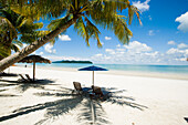 Malaysia, Pantai Cenang (Cenang Strand); Pulau Langkawi, Liegestühle unter Sonnenschirm am weißen Sandstrand mit Palmen und Blick aufs blaue Meer