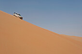 VAE, Abu Dhabi, Geländewagen fährt steile Sanddüne hinunter; Liwa