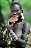 Portrait of a Mursi tribal woman displaying pierced ear lobes & lower lip (to hold a traditional 'debhi a tugoin' - lip plate) and scar tattoos. Makki / South Omo / Southern Nations, Nationalities & People's Region (Ethiopia).